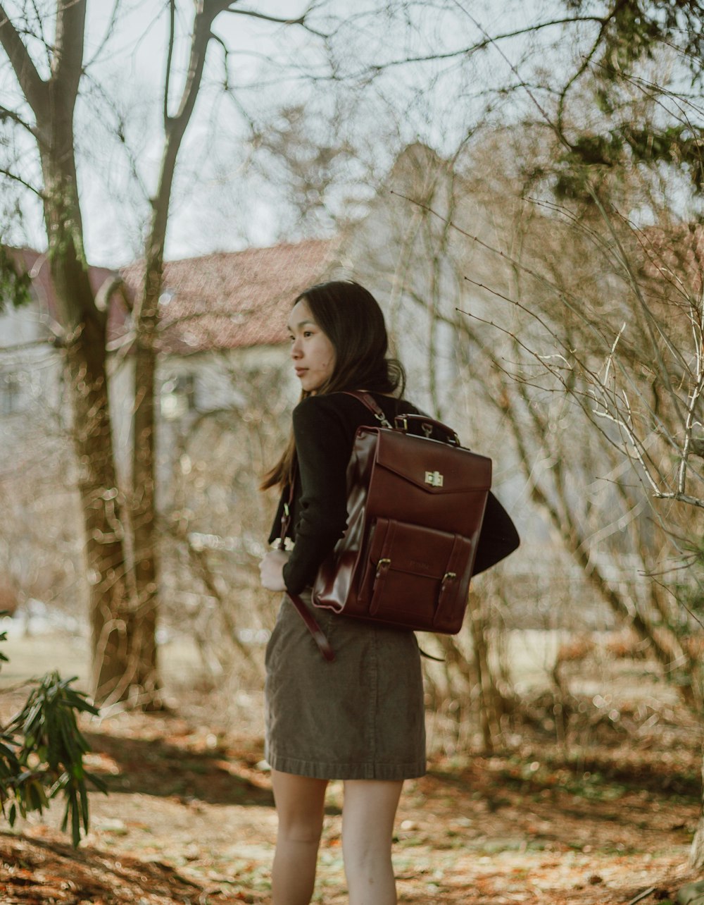 woman in black jacket and white skirt standing near brown trees during daytime