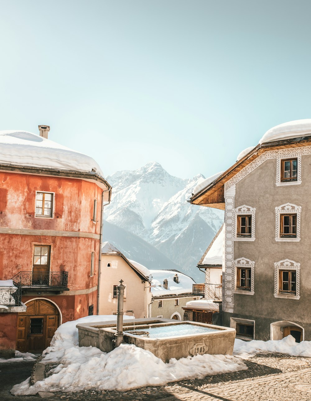 brown concrete building near snow covered mountain during daytime