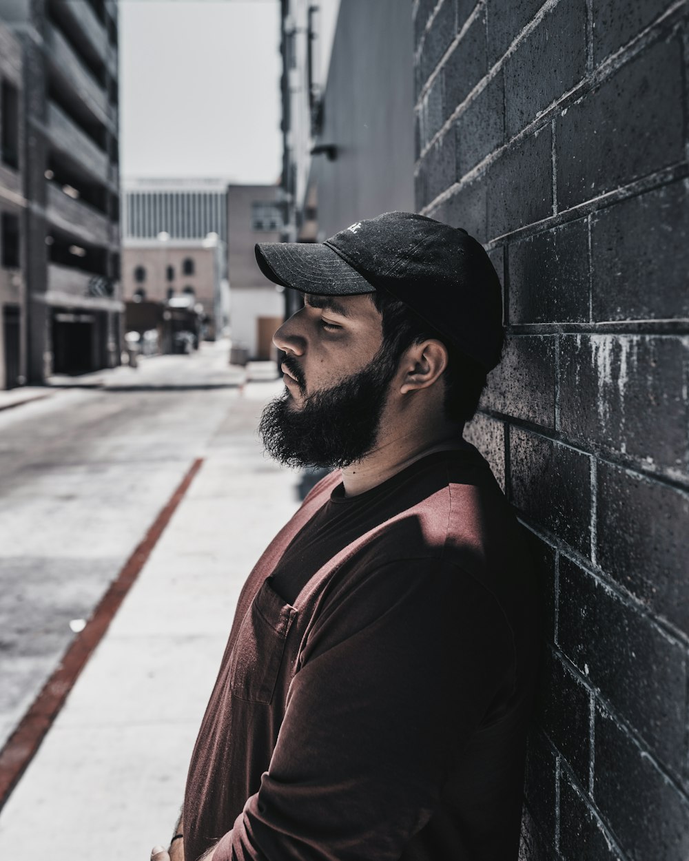 man in brown jacket and black hat standing beside gray concrete wall during daytime