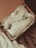 A pair of white sneakers is neatly placed inside a cardboard shoe box. The shoes are surrounded by crumpled white tissue paper, which lines the box. The exterior of the box is slightly ajar, revealing the soft texture of a waffle-patterned brown blanket underneath.