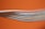 Several colored cables are stacked closely together against a bright orange background. The cables, including white, blue, and red, create a layered texture. Some text is visible on one of the cables, though it is partially blurred.