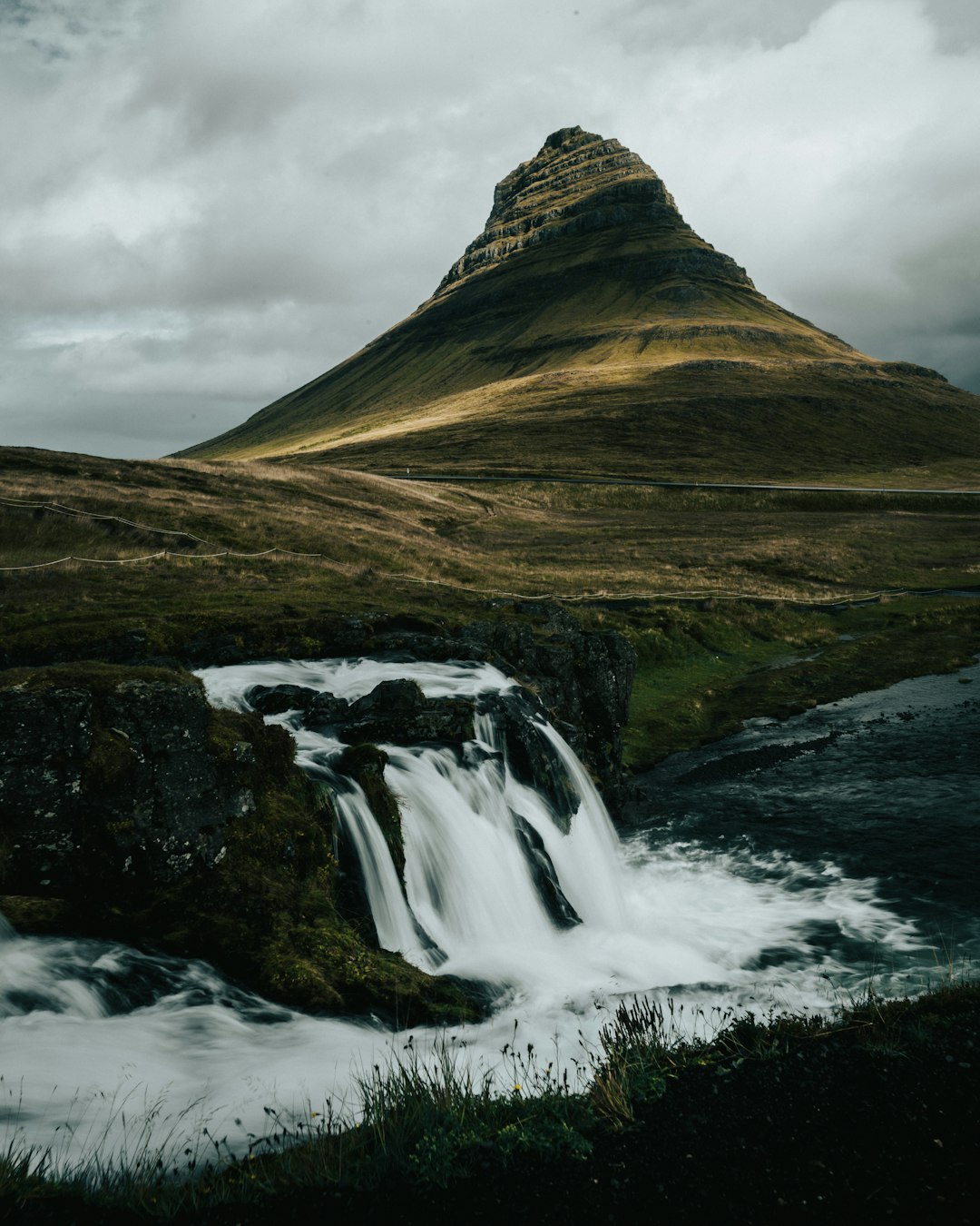 waterfalls near brown mountain under white clouds during daytime