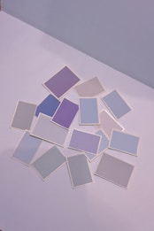 A collection of variously colored rectangular cards is scattered on a flat surface. The colors are primarily soft, including shades of purple, blue, and gray, each card distinct yet muted and pastel in appearance.