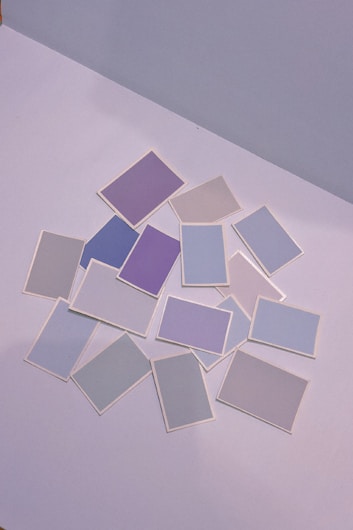 A collection of variously colored rectangular cards is scattered on a flat surface. The colors are primarily soft, including shades of purple, blue, and gray, each card distinct yet muted and pastel in appearance.
