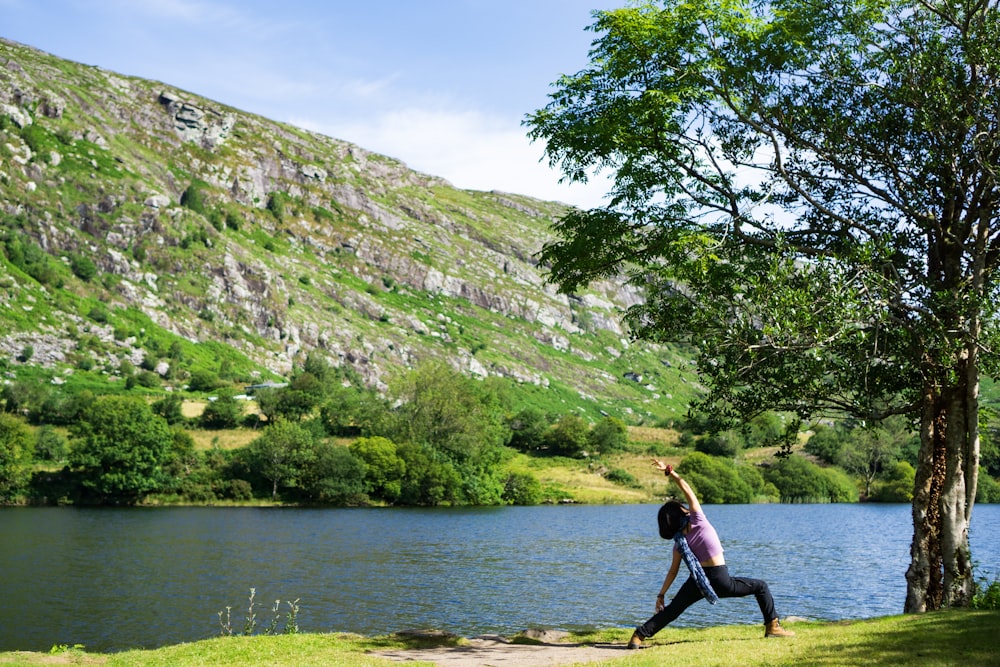 woman in black tank top and black leggings sitting on tree branch near lake during daytime