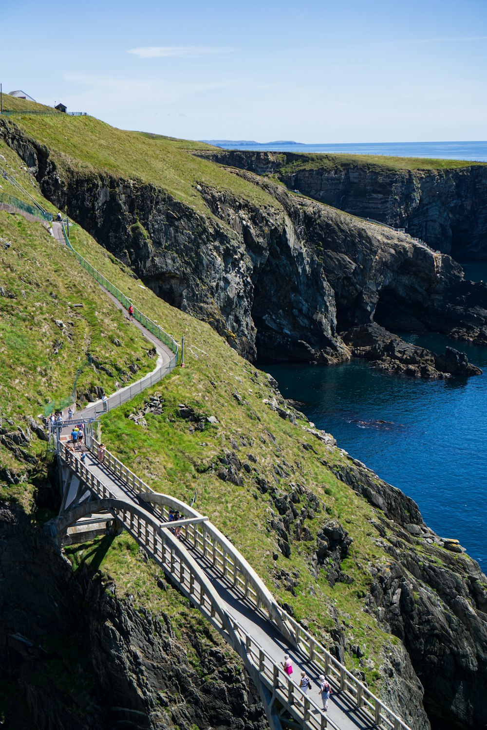 white wooden bridge on green mountain near blue sea during daytime