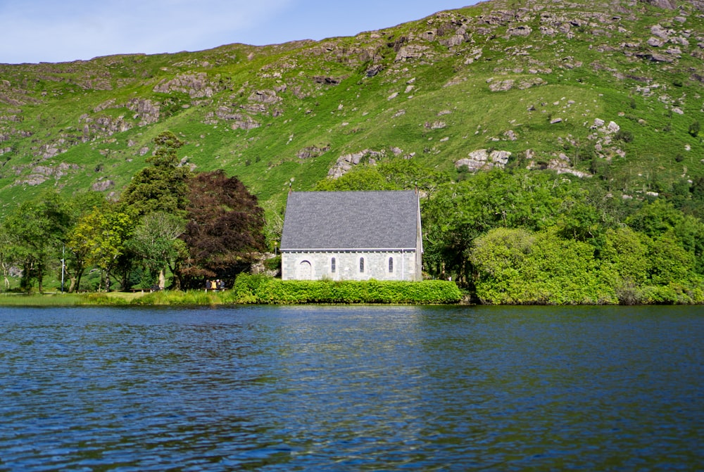 gray concrete house near green grass covered hill and body of water during daytime