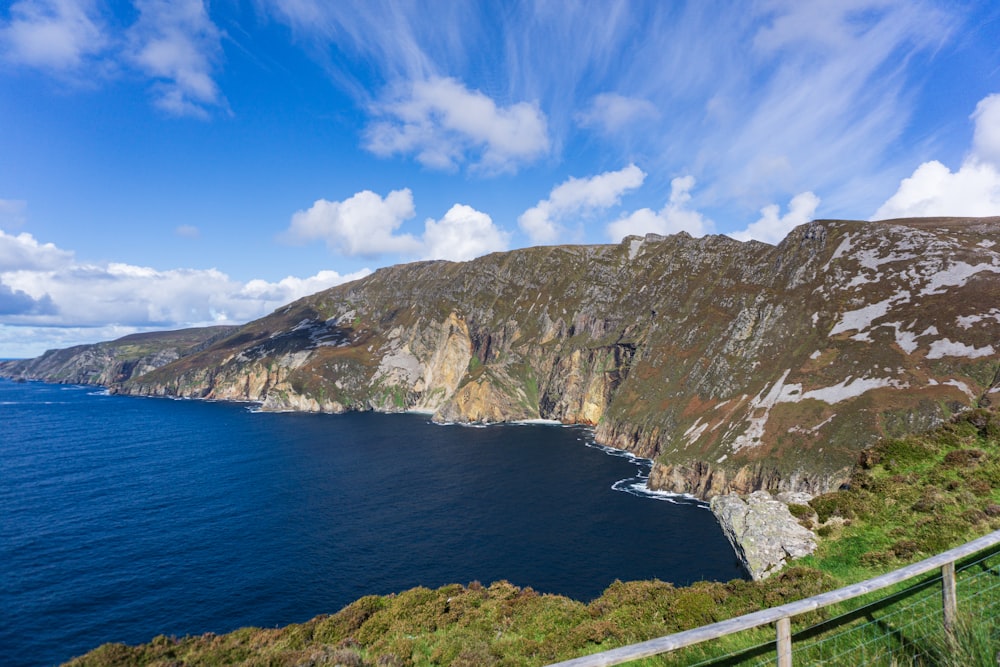 green and brown mountain beside blue sea under blue sky during daytime