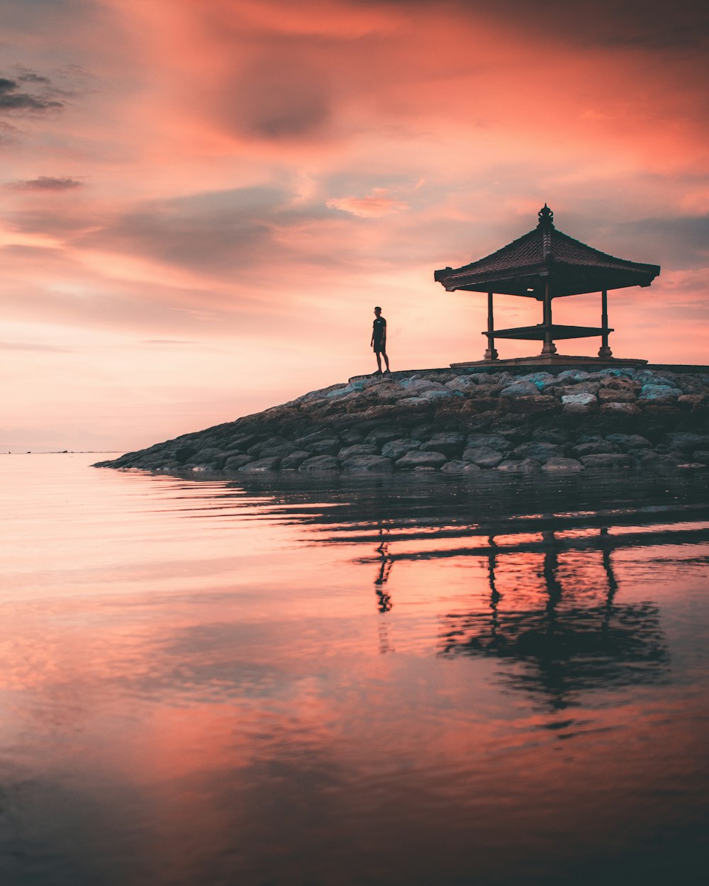 person standing on rock formation near body of water during sunset