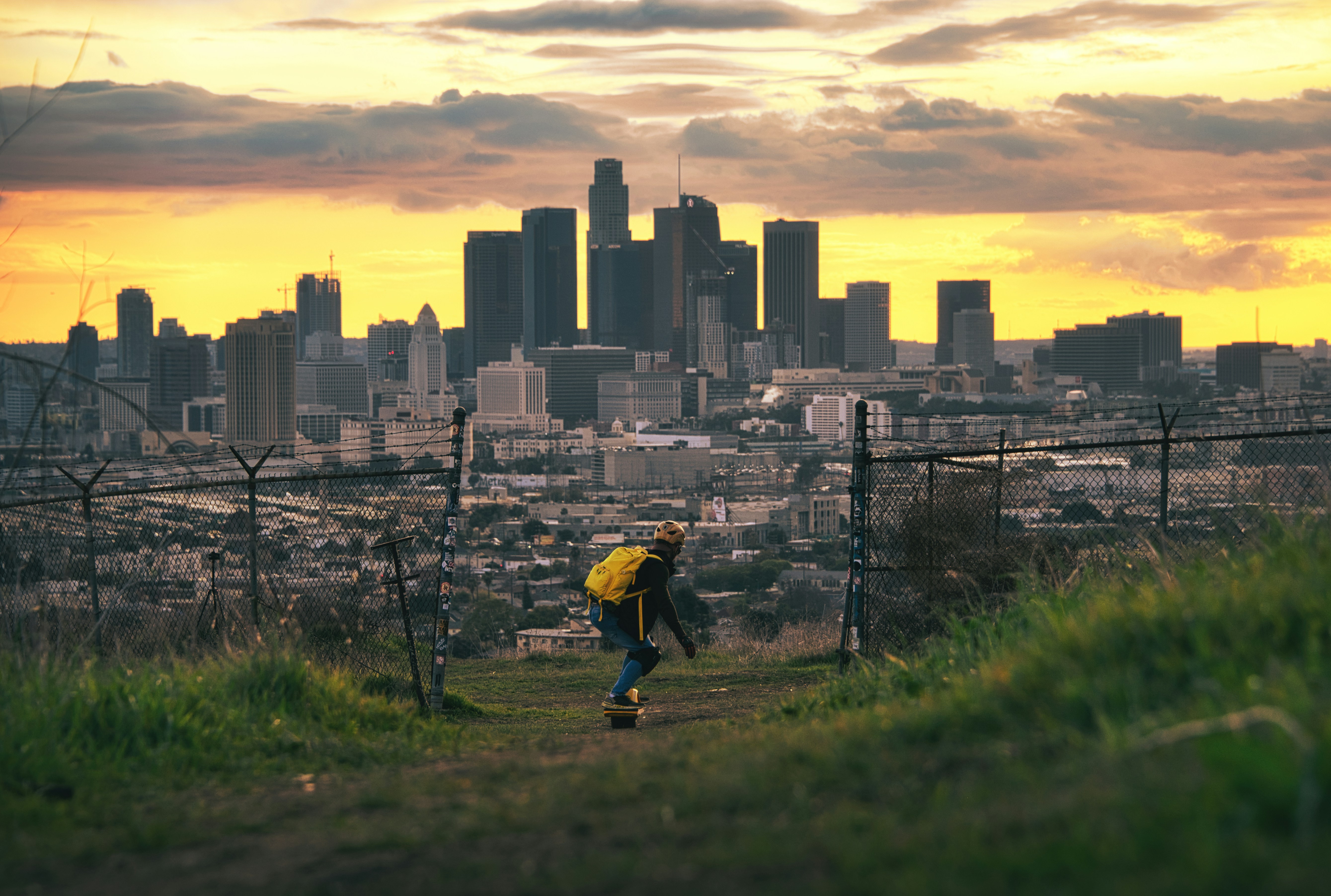 person in yellow jacket and black pants walking on green grass field during daytime
