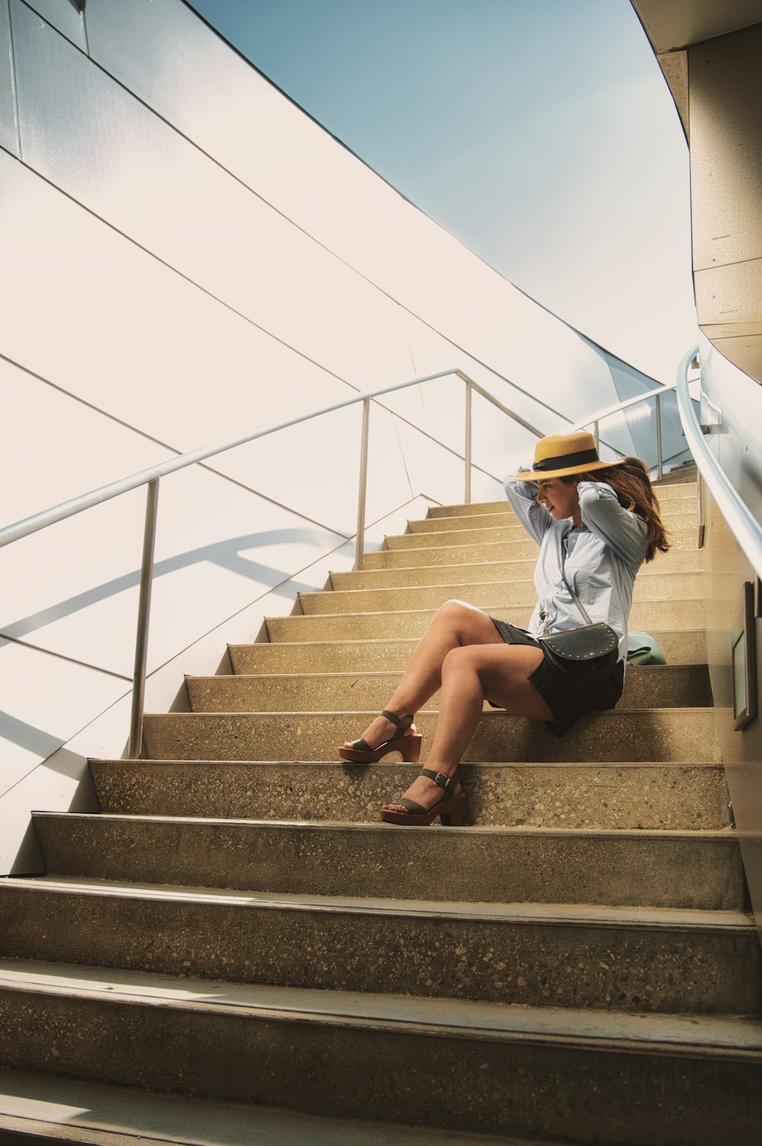 woman in white shirt and black shorts sitting on gray concrete staircase