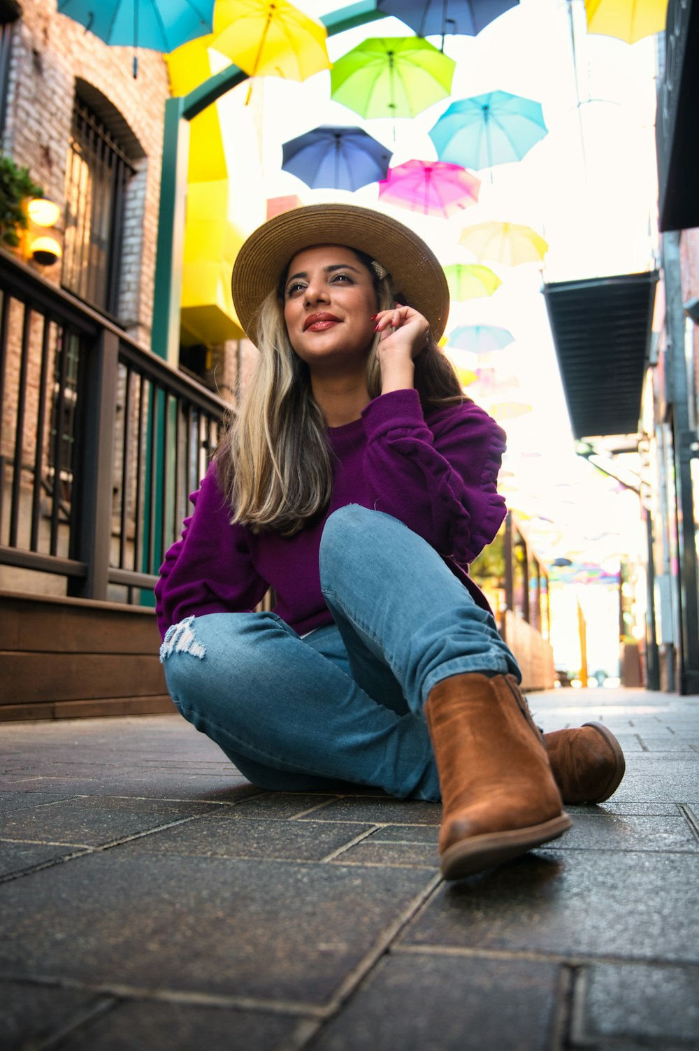 woman in purple jacket and blue denim jeans sitting on sidewalk during daytime