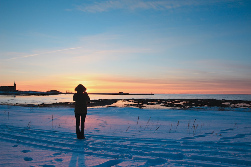 silhouette of person standing on snow covered ground during sunset