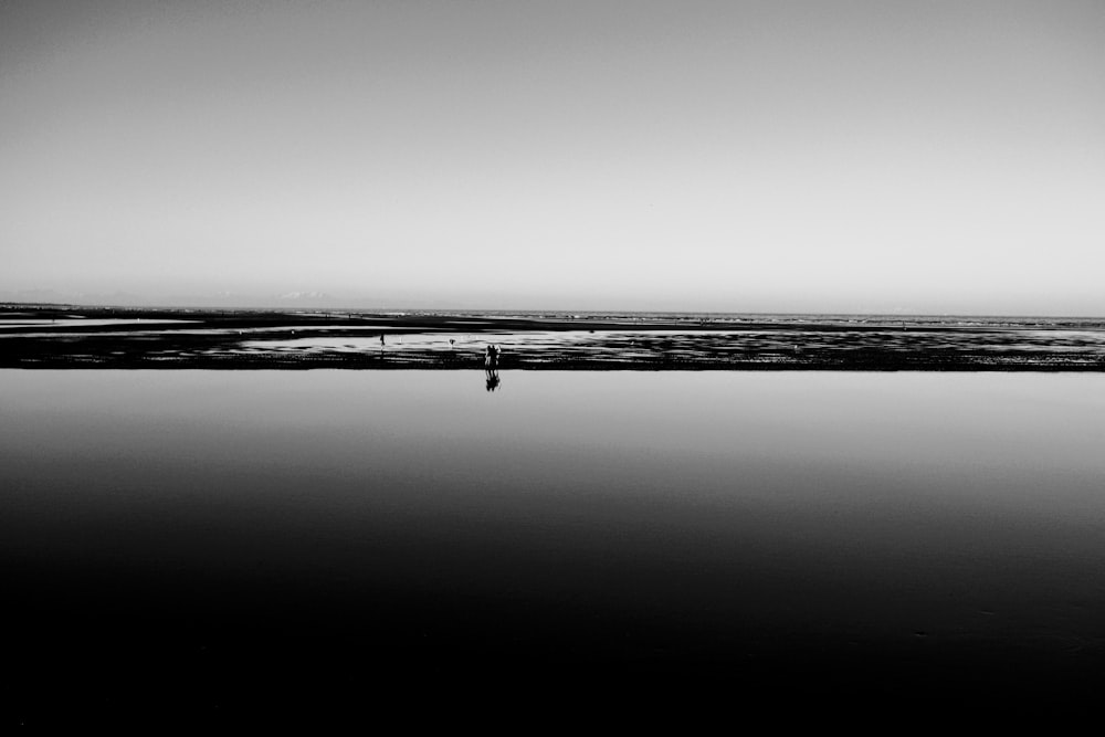 해변을 걷는 사람의 그레이스케일 사진