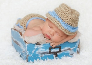 baby in white knit cap lying on blue and white textile
