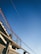 A metal staircase with railings is seen against a clear blue sky. The structure includes straight lines and geometric patterns, with a wire or cable extending across the top corner.