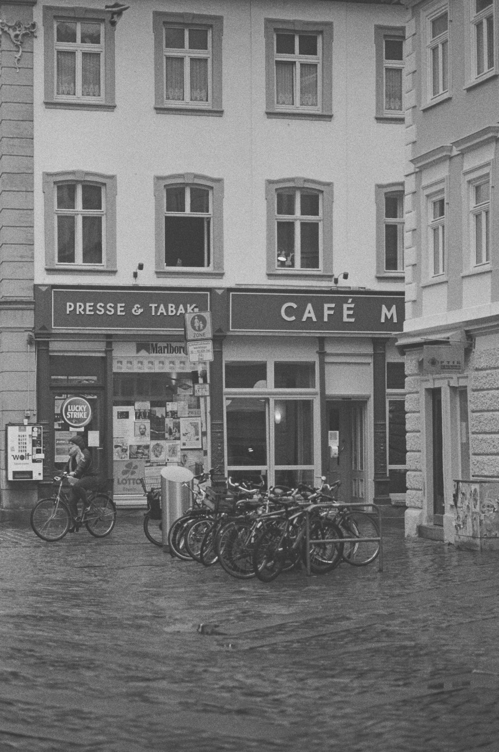 grayscale photo of bicycles parked beside building