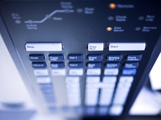 A detailed close-up of a control panel with various labeled buttons, including prominent ones that say Stop, Prep Run, and Start. The panel appears to be part of a technical or scientific instrument, with other buttons labeled Oven, Valve 6, and more. The image has a soft focus and a slight blue tint.