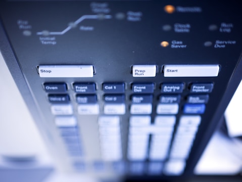 A detailed close-up of a control panel with various labeled buttons, including prominent ones that say Stop, Prep Run, and Start. The panel appears to be part of a technical or scientific instrument, with other buttons labeled Oven, Valve 6, and more. The image has a soft focus and a slight blue tint.