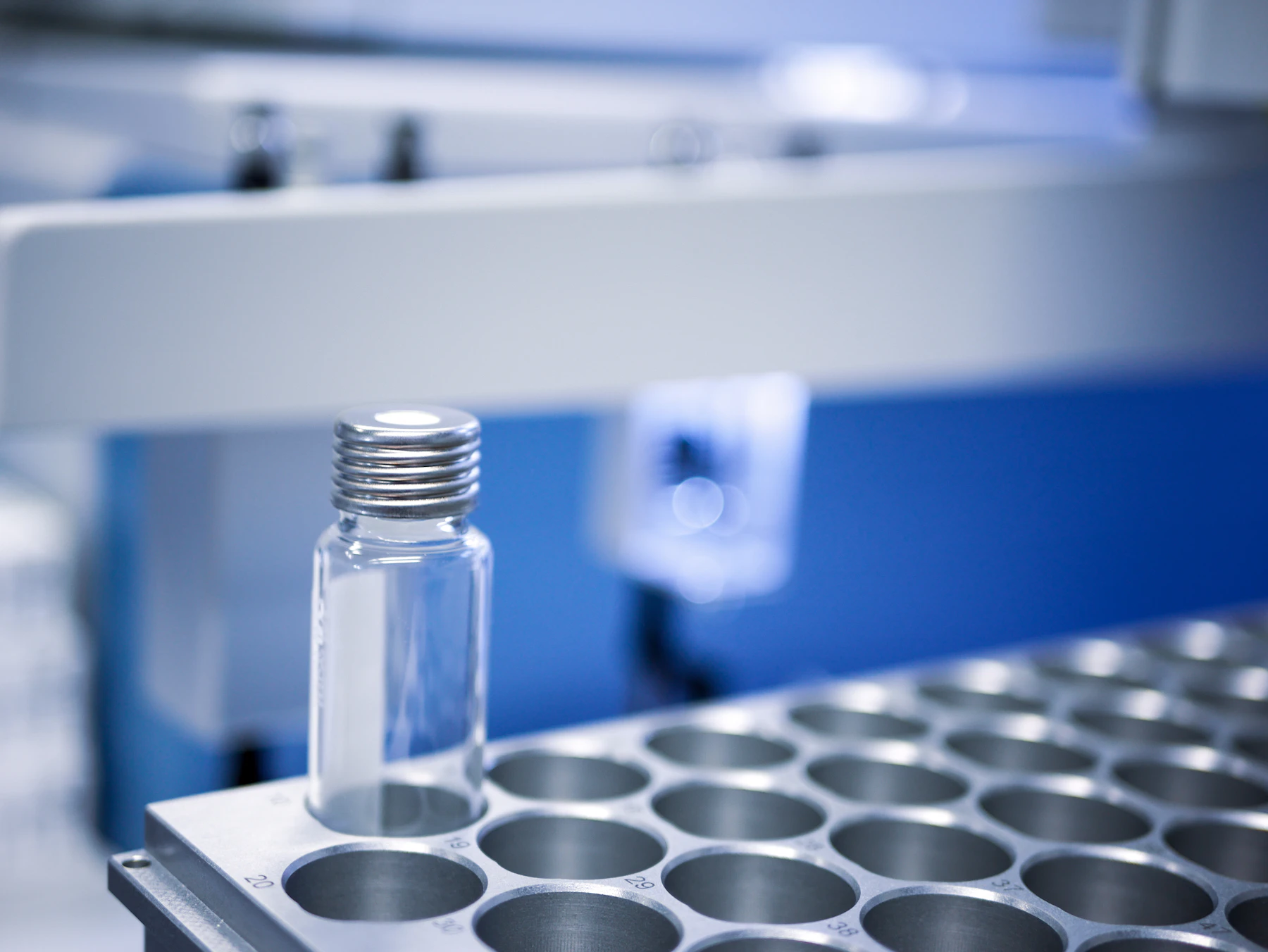 A single glass vial standing in a steel rack on a blue-lit bench