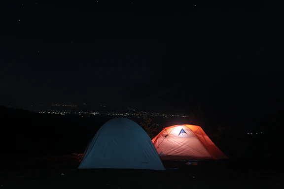 A cozy camping scene at dusk with a tent softly lit from inside under a starry sky.