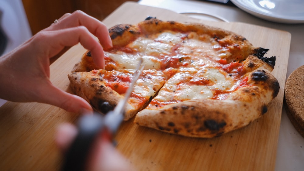 person slicing pizza on brown wooden table