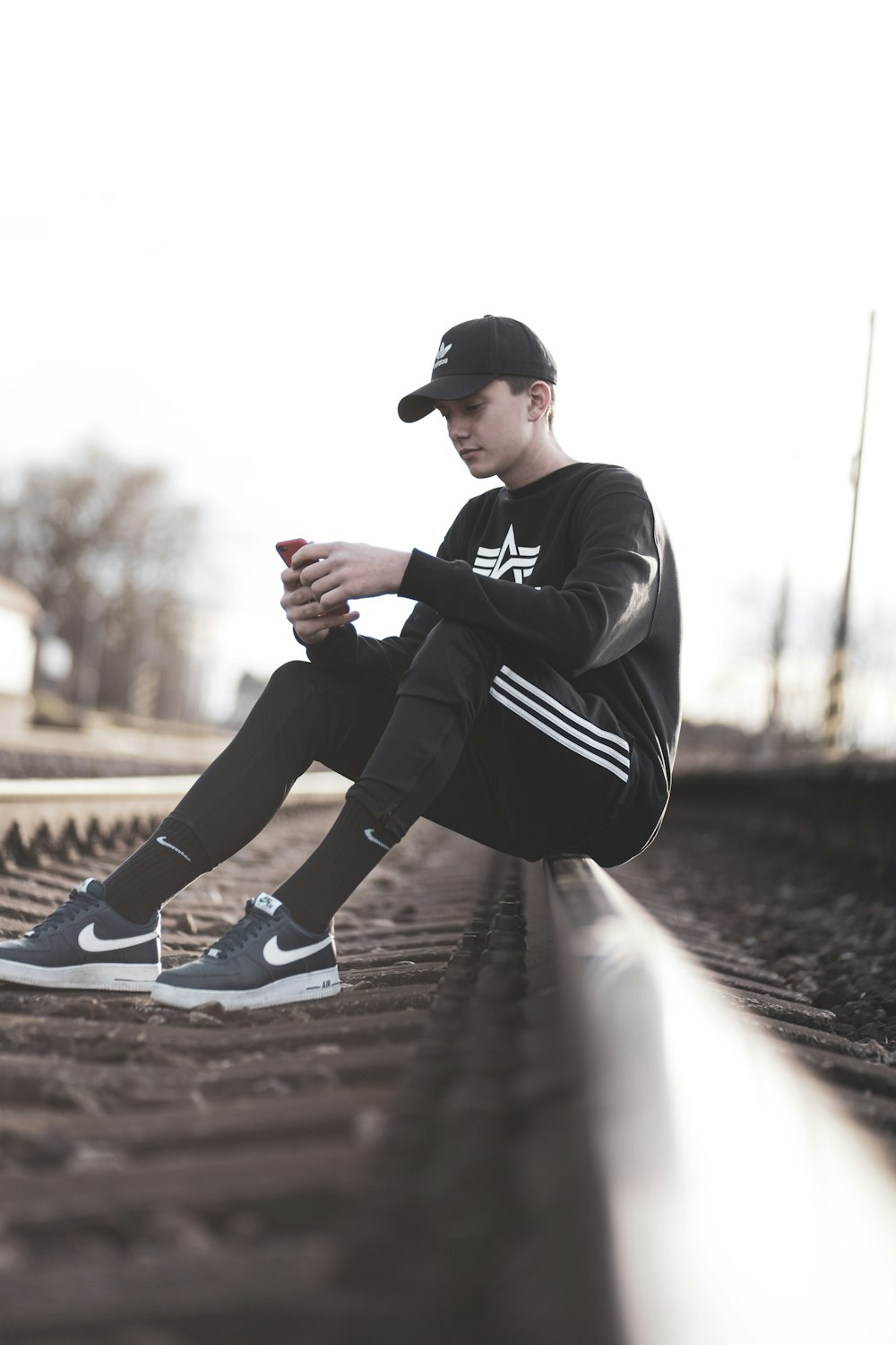 man in black and white adidas sweater and black pants sitting on train rail  during daytime photo – Free Bratislava Image on Unsplash