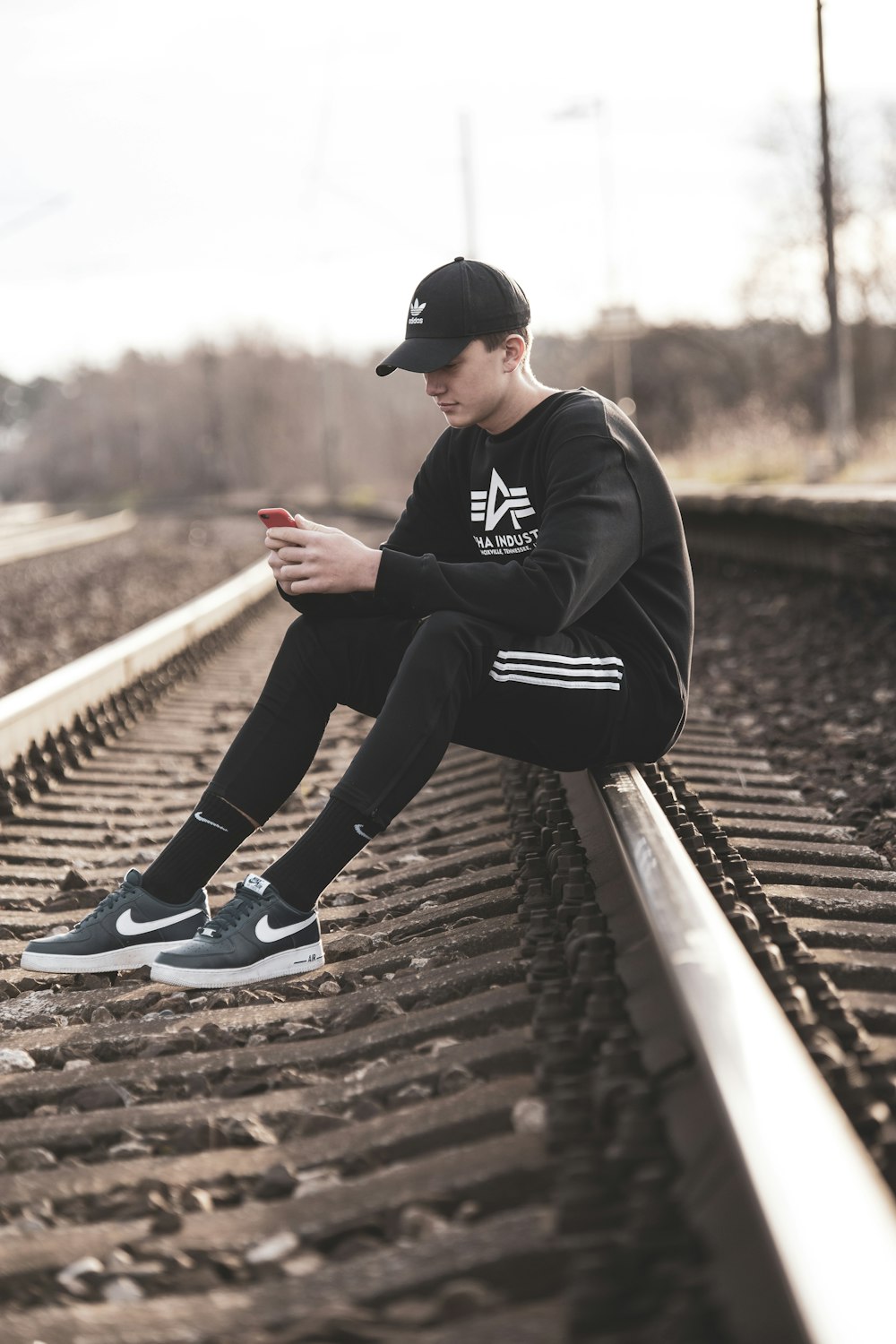 man in black hoodie and black pants sitting on train rail during daytime