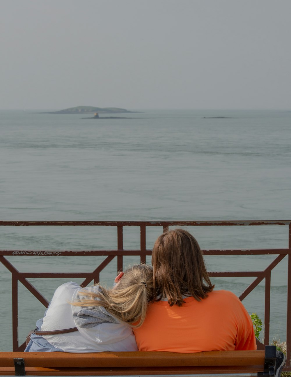 woman in white long sleeve shirt sitting on red metal railings near body of water during