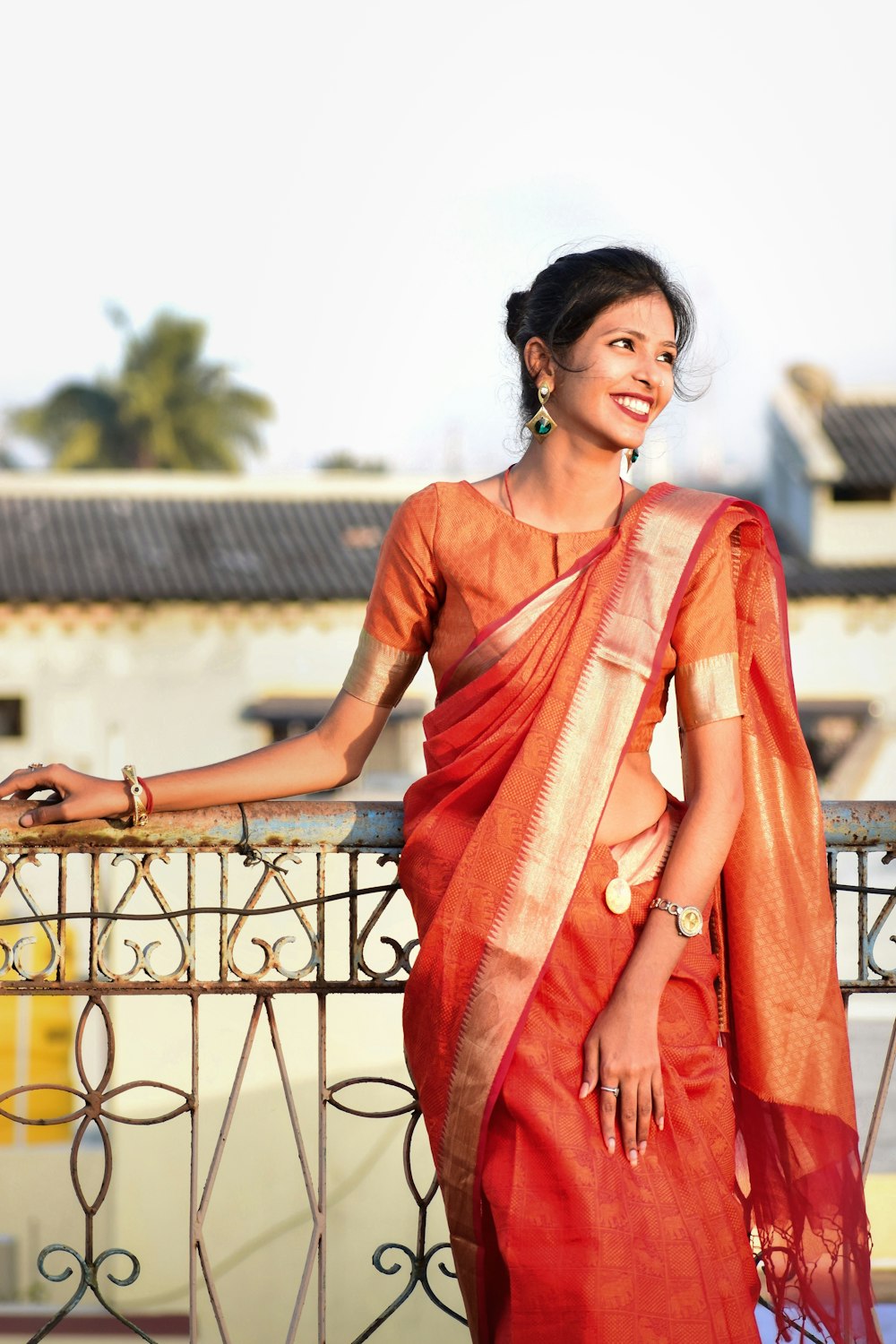 uma mulher em um sari laranja em pé em uma varanda