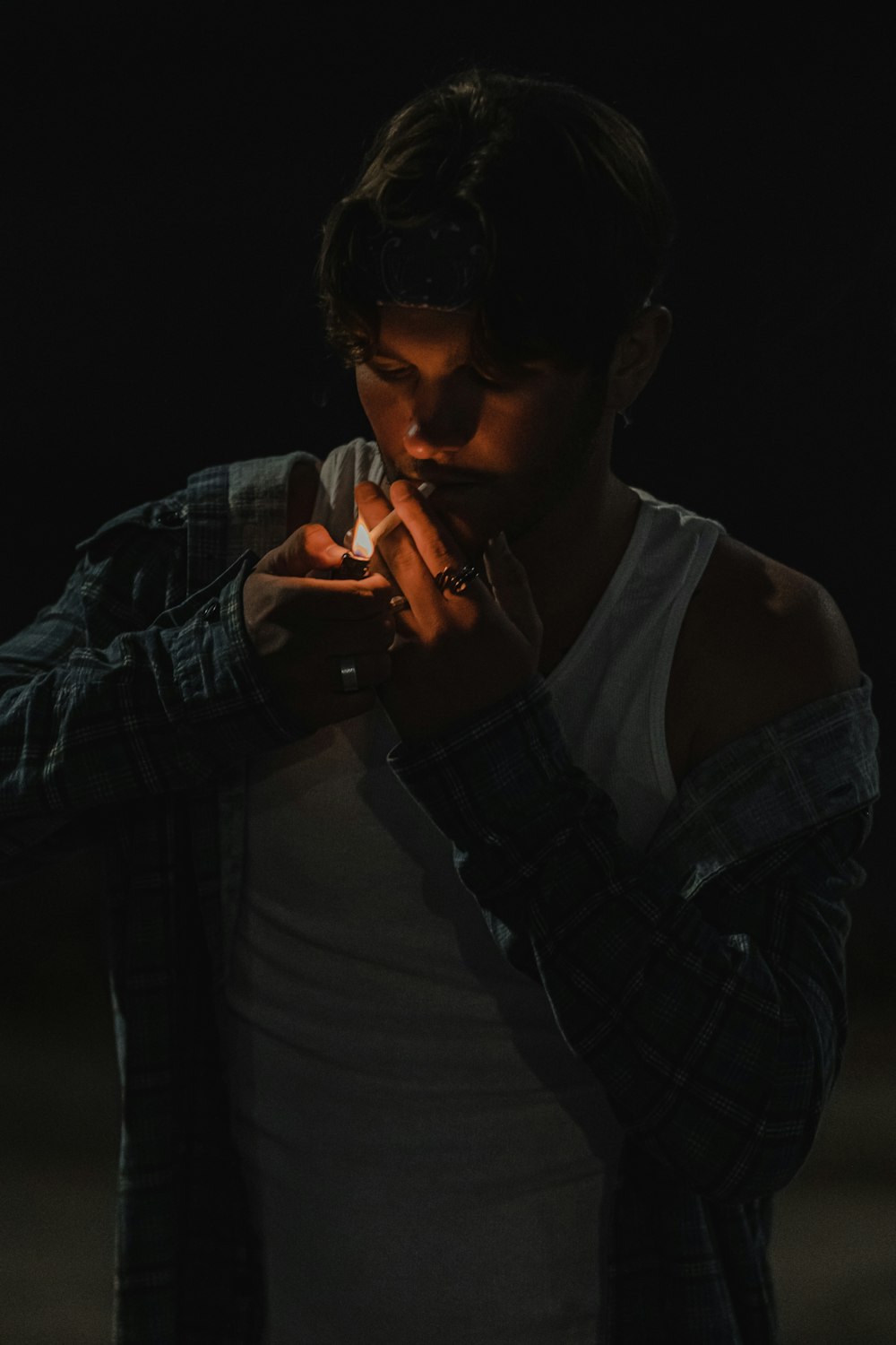 man in white tank top and black and gray plaid jacket smoking cigarette