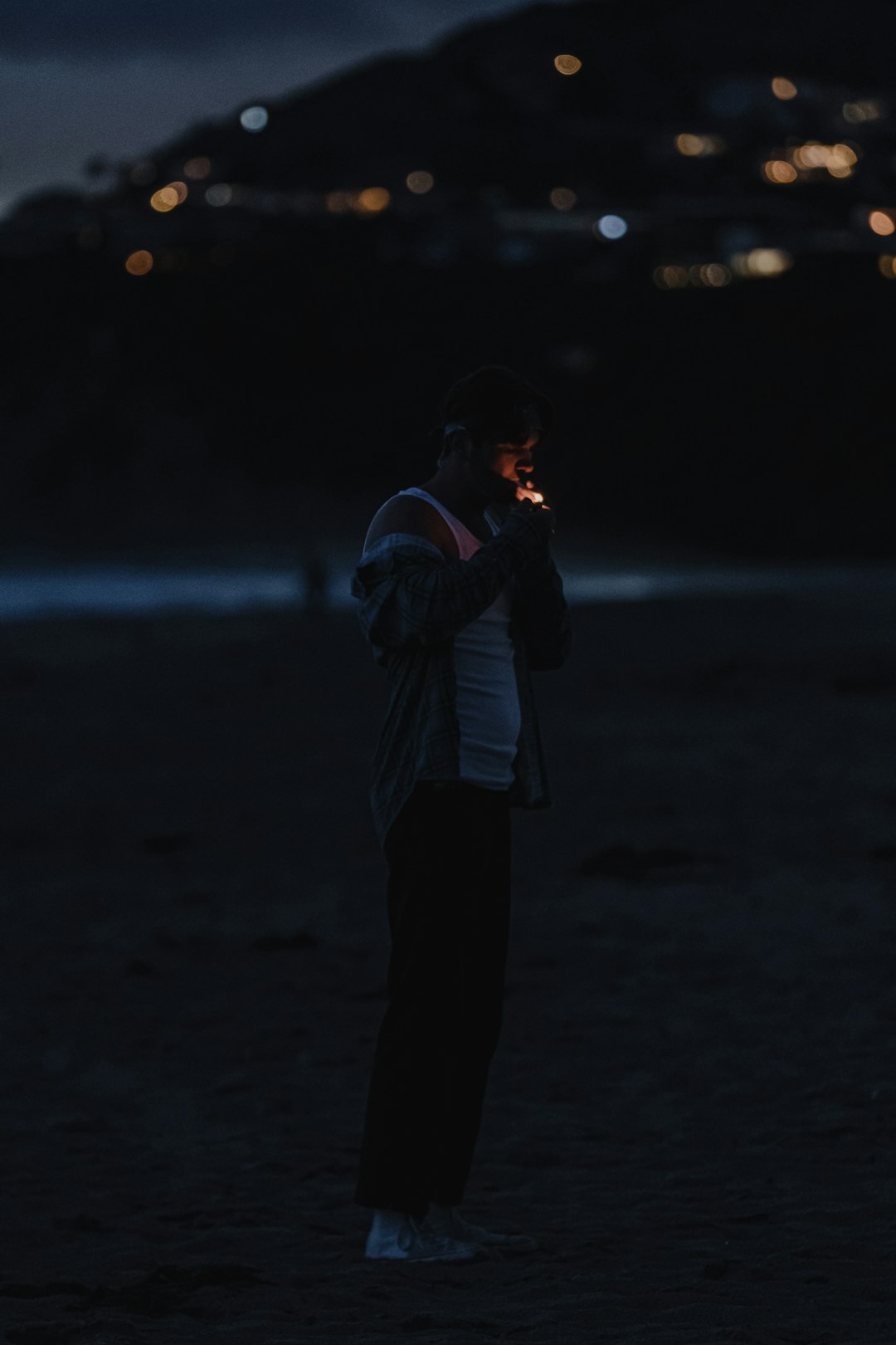 man in white dress shirt and black pants standing on gray sand during night time