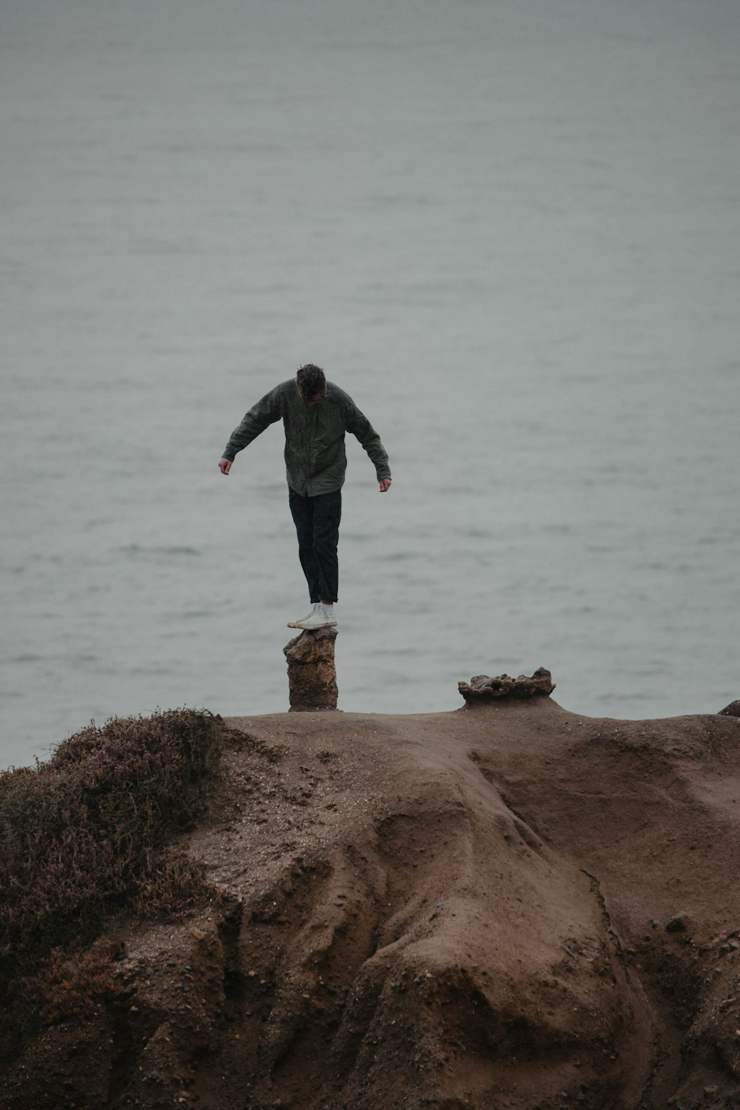 man in black jacket standing on brown rock