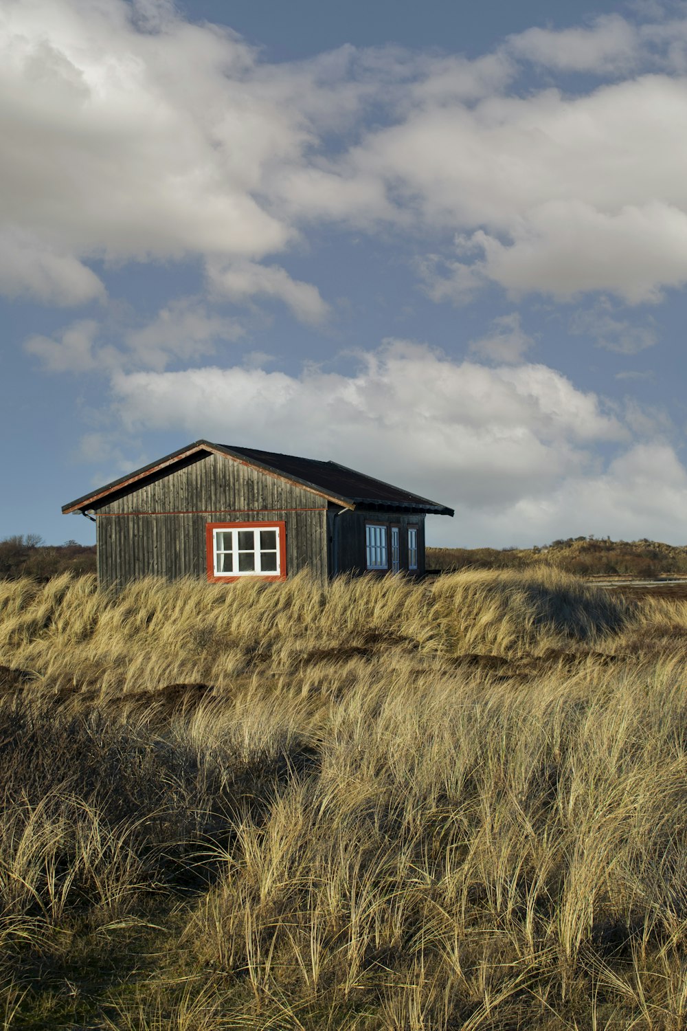 Braunes Holzhaus auf braunem Grasfeld unter weißen Wolken und blauem Himmel tagsüber