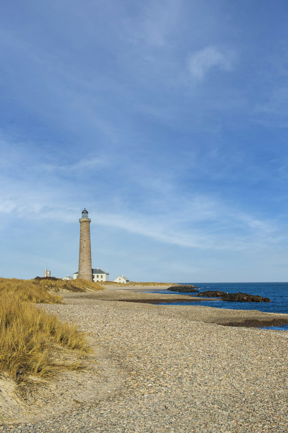 white and brown lighthouse on brown sand near body of water during daytime