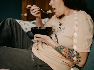 woman in white floral long sleeve shirt holding black ceramic mug and eating, looks sad, frustrated
