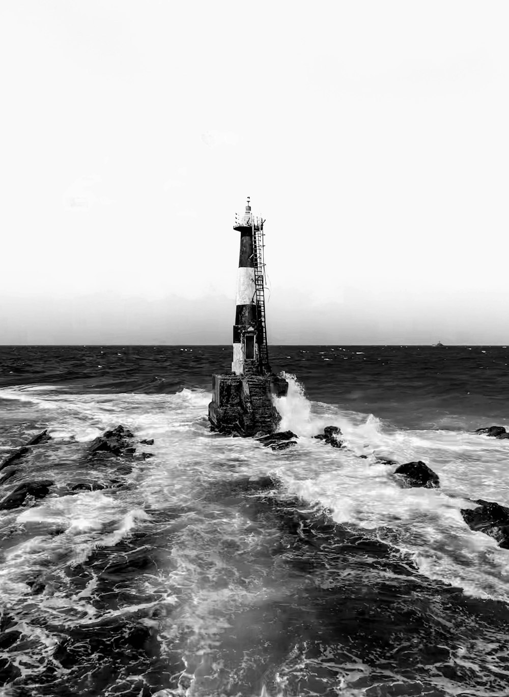 grayscale photo of lighthouse on rock formation