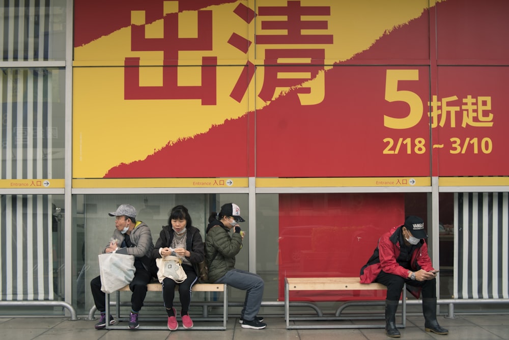 people sitting on bench near red wall