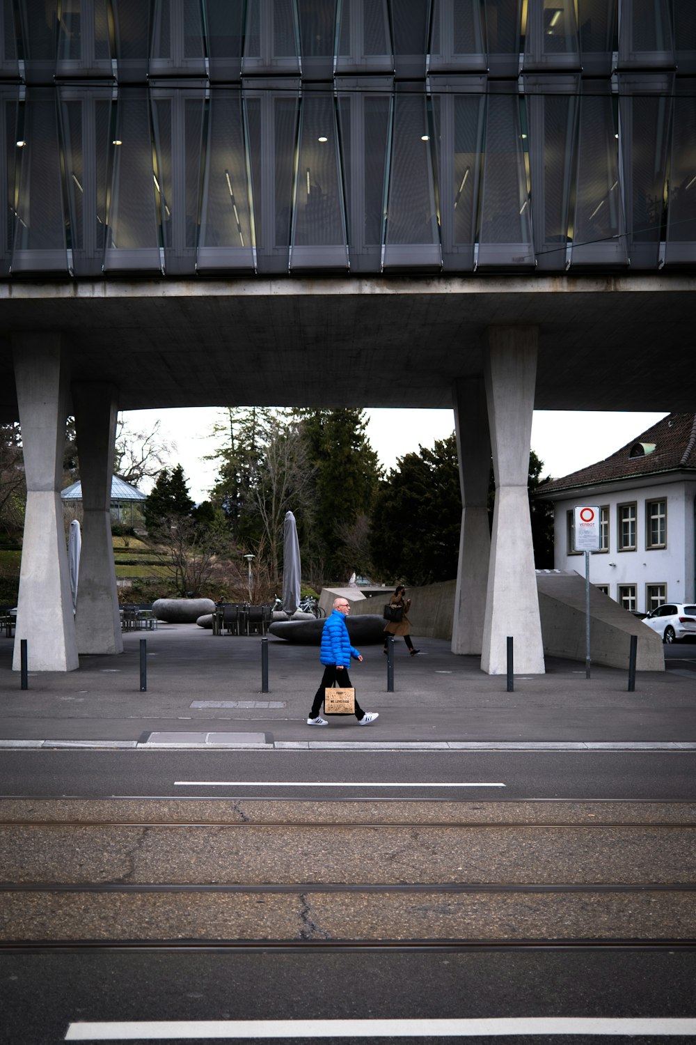 man in blue jacket and black pants walking on sidewalk during daytime