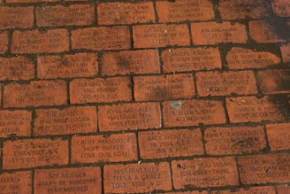 A series of engraved red bricks with various personal messages and dedications. The inscriptions often include references to the Boston Red Sox and expressions of loyalty and fandom, as well as dedications to family and friends.