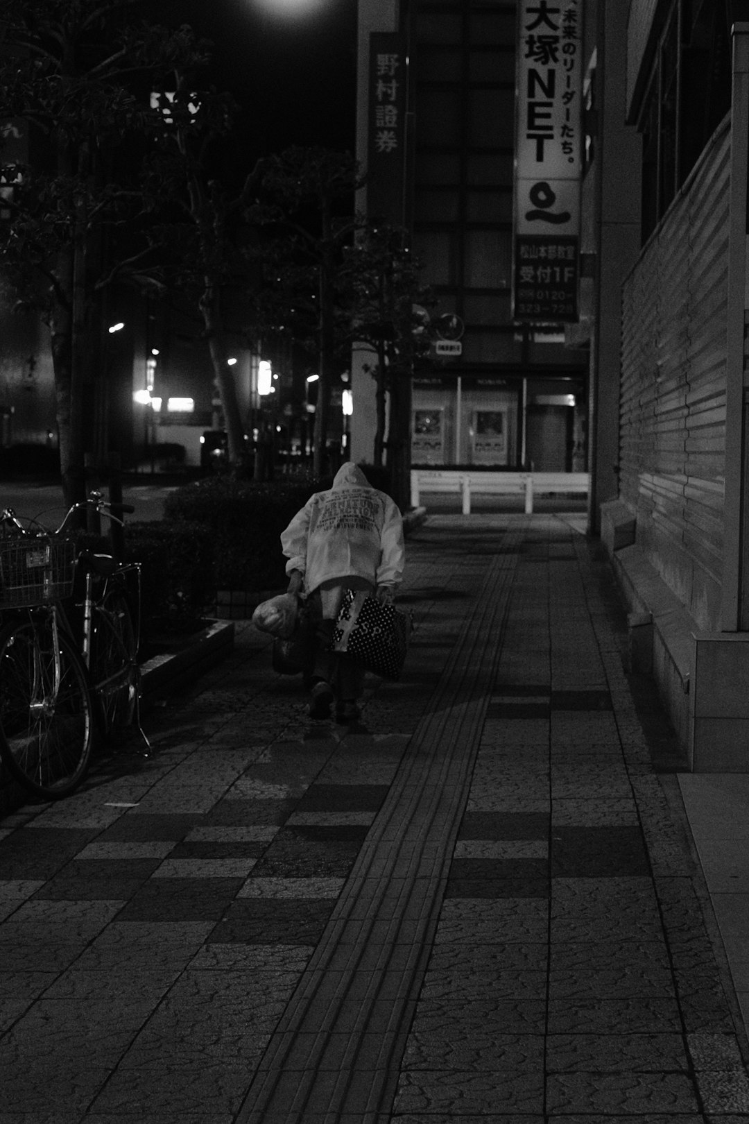 grayscale photo of man sitting on bench near road
