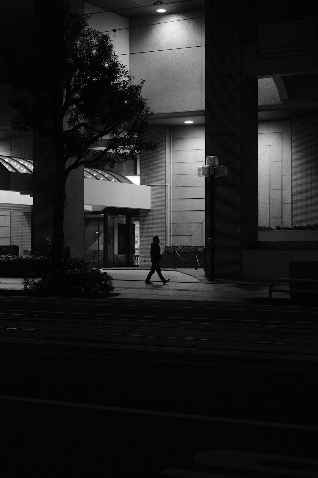 grayscale photo of woman walking on sidewalk