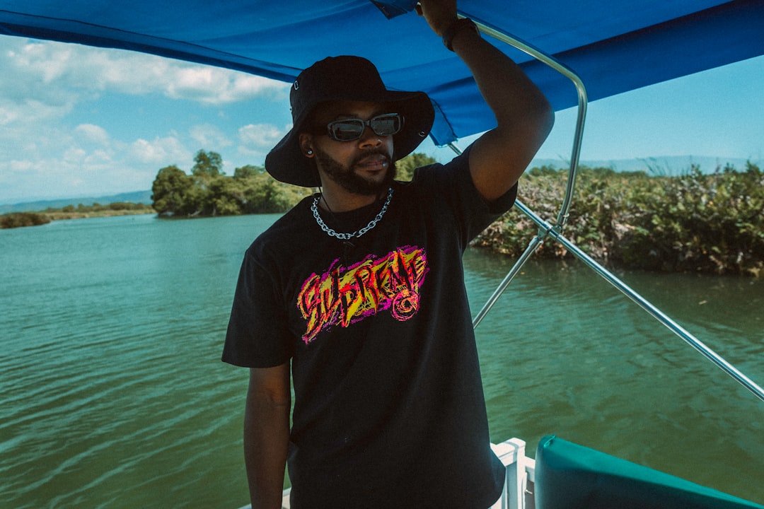 man in black crew neck t-shirt wearing black hat standing on boat during daytime