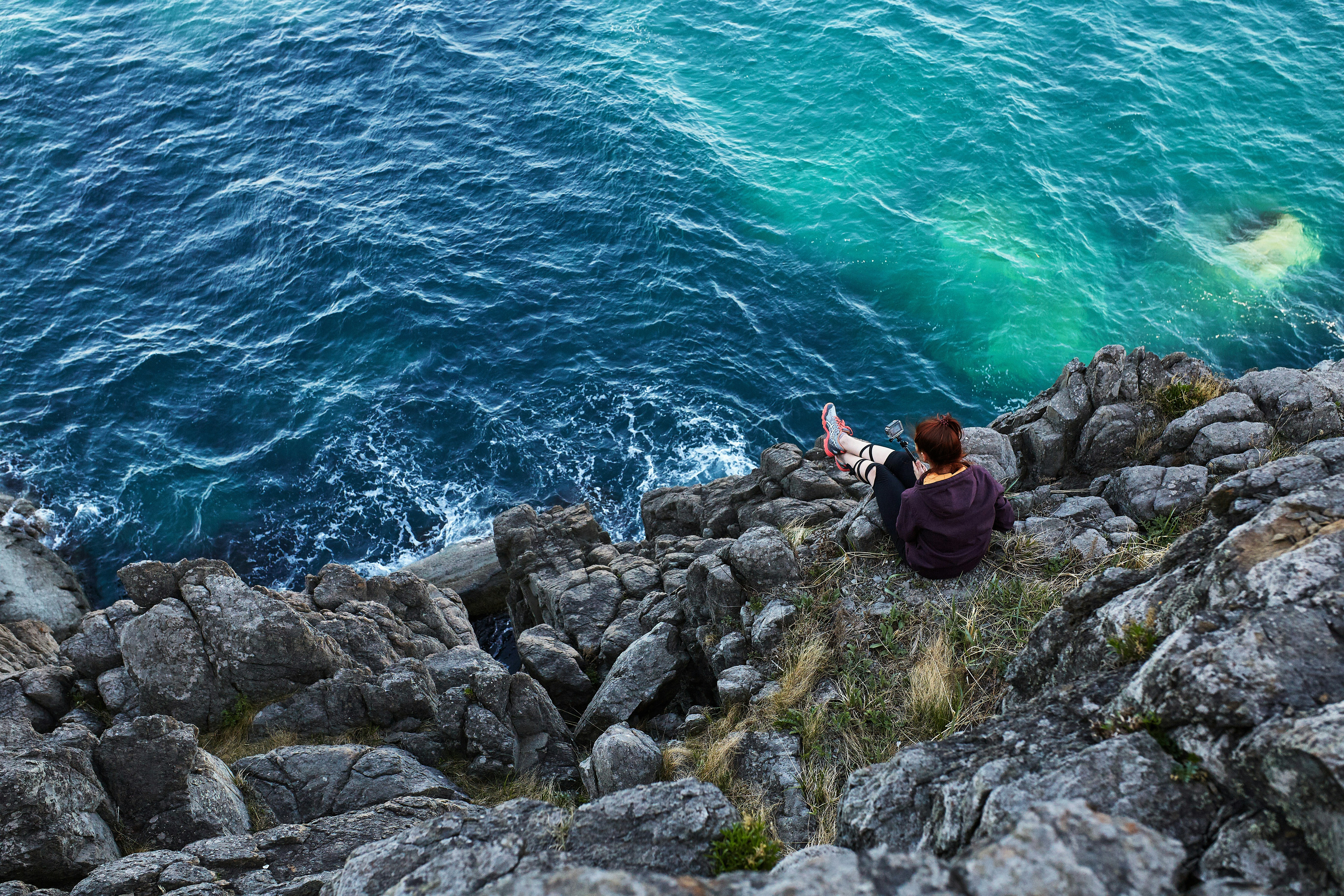 woman in black jacket and black pants sitting on rock by the sea during daytime