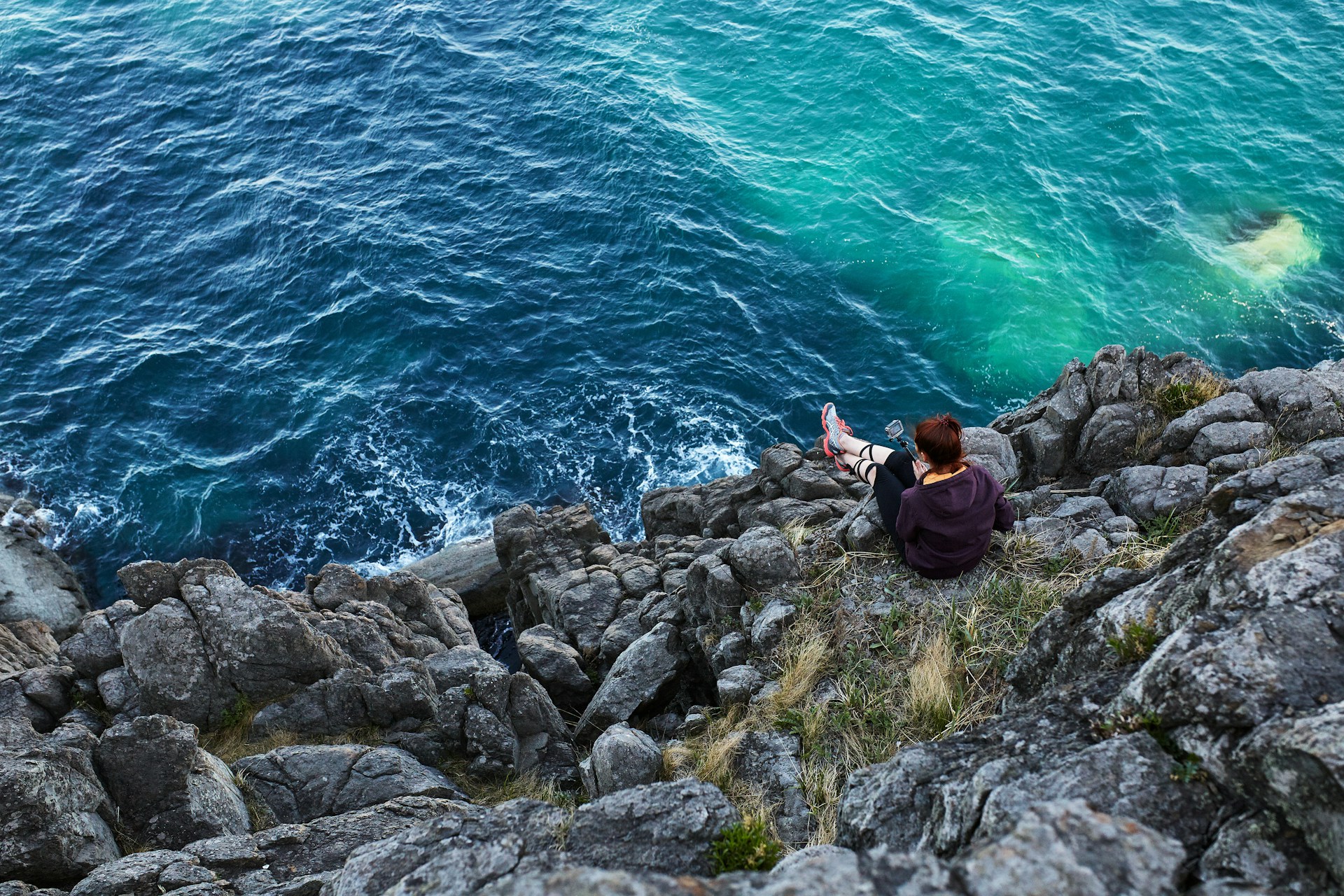 woman in black jacket and black pants sitting on rock by the sea during daytime