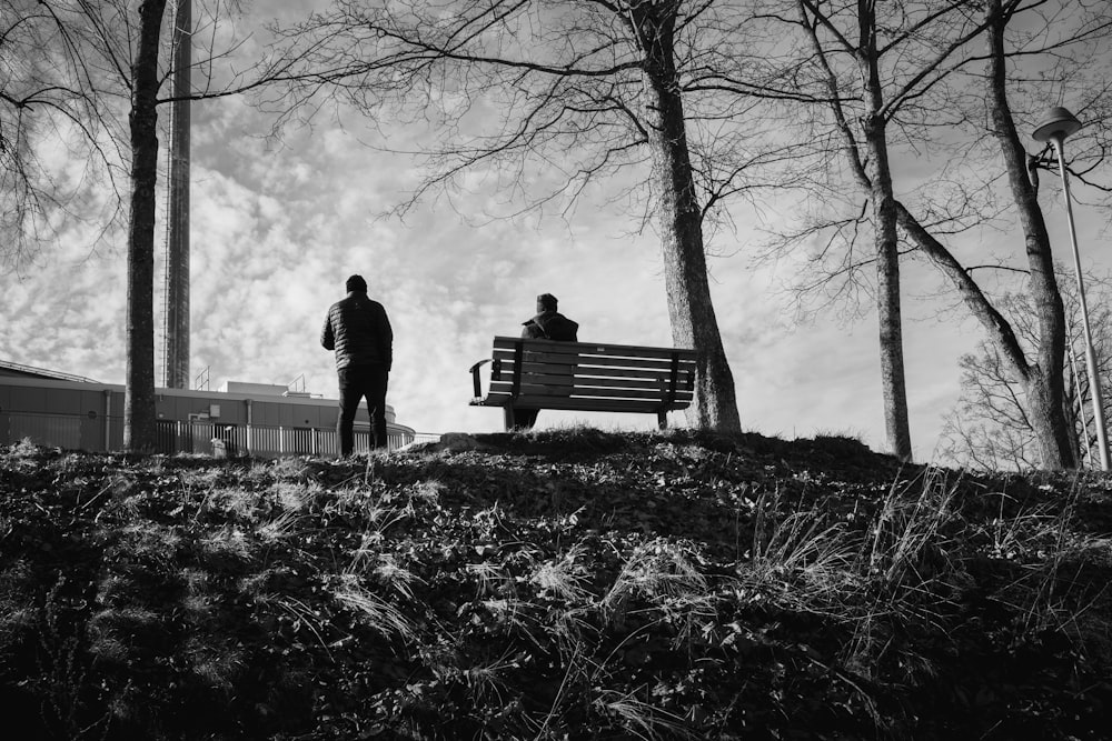 grayscale photo of man standing near bench