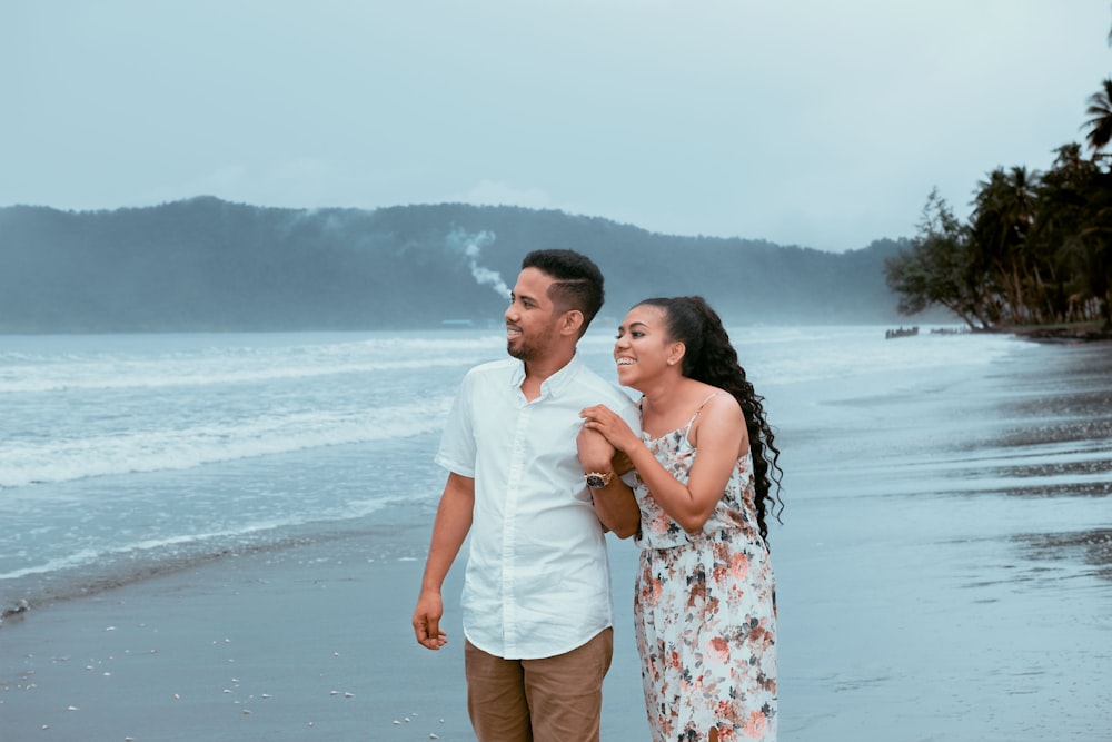 man in white dress shirt kissing woman in white floral dress on beach during daytime