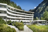 white concrete building near green trees and mountain during daytime
