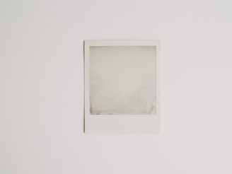 A blank Polaroid photograph is positioned against a plain white background. The image inside the photograph is not developed or visible, resulting in an empty, grey-ish square within the white frame.