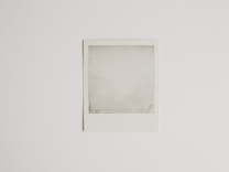 A blank Polaroid photograph is positioned against a plain white background. The image inside the photograph is not developed or visible, resulting in an empty, grey-ish square within the white frame.